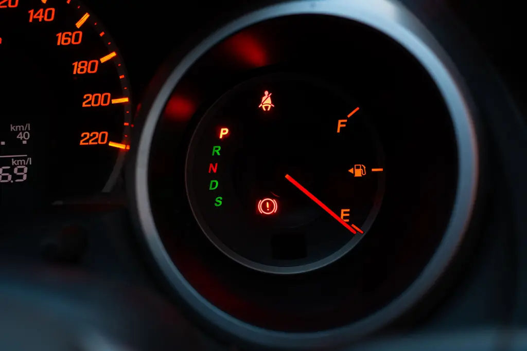 Close-up of a car dashboard showing an illuminated brake warning light, seat belt indicator, and low fuel gauge.