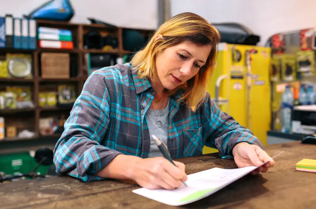 Woman in a plaid shirt reviewing and writing on paperwork at a counter in an automotive shop.